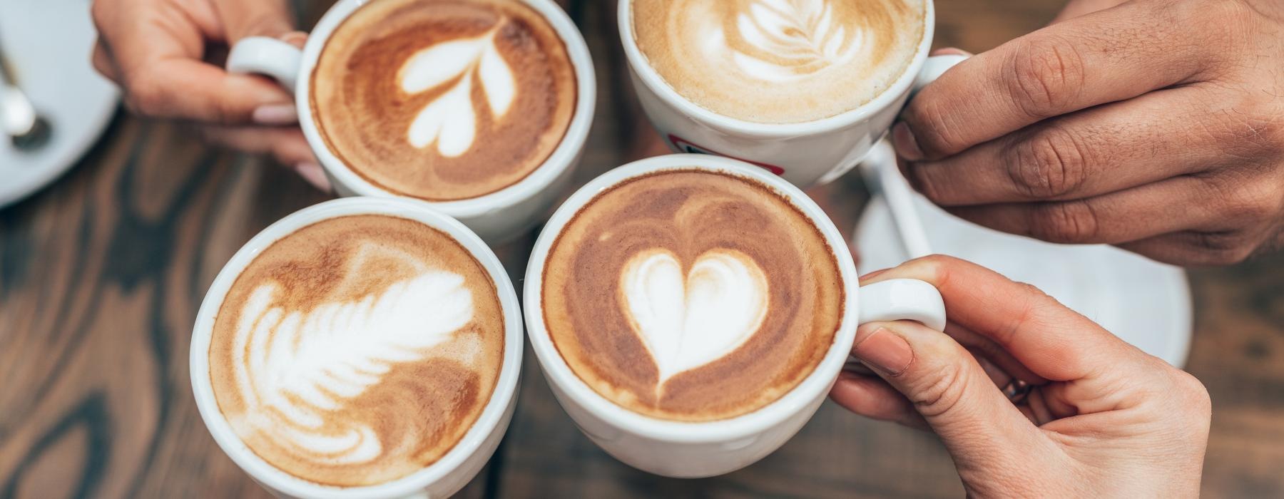 a group of hands holding cups of coffee with foam on the top